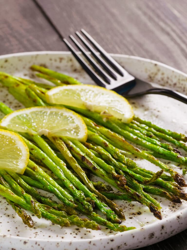 Charred grilled asparagus topped with lemon sliced on a plate.