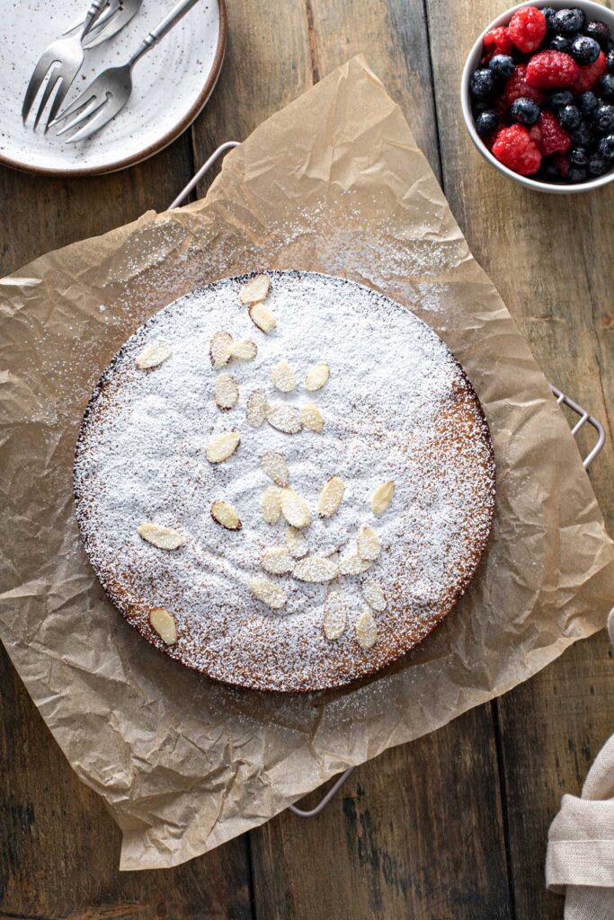 A whole cake dusted with powdered sugar and topped with sliced toasted almonds.