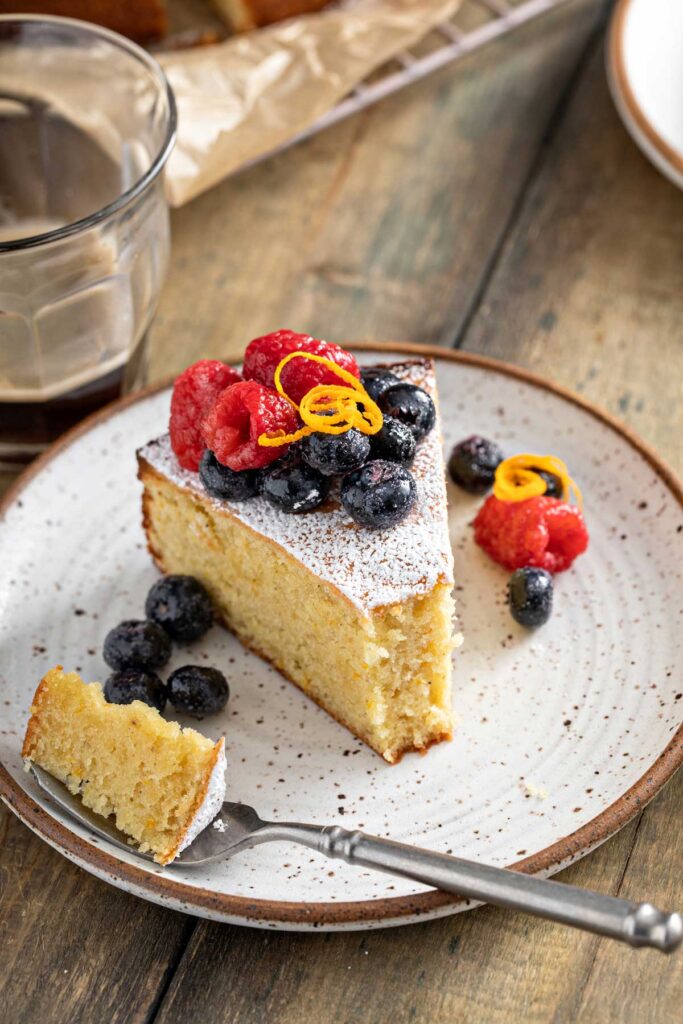 A piece of cake has been taken out from a slice of almond cake served with fresh berries on a plate.