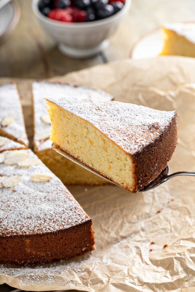 Slice of fluffy almond cake lifted from a piece of parchment paper