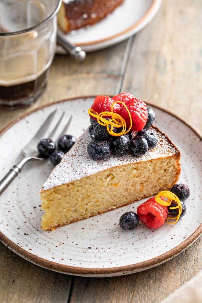 A sliced of simple almond cake topped with fresh berries on a plate.