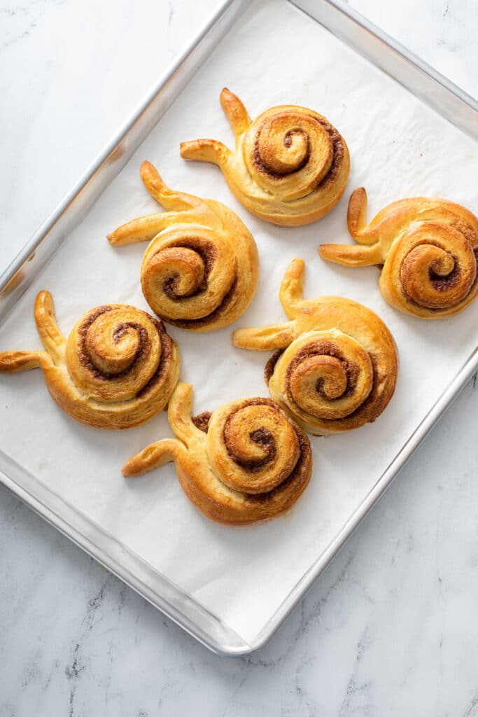 six golden brown bunny cinnamon rolls on a baking tray