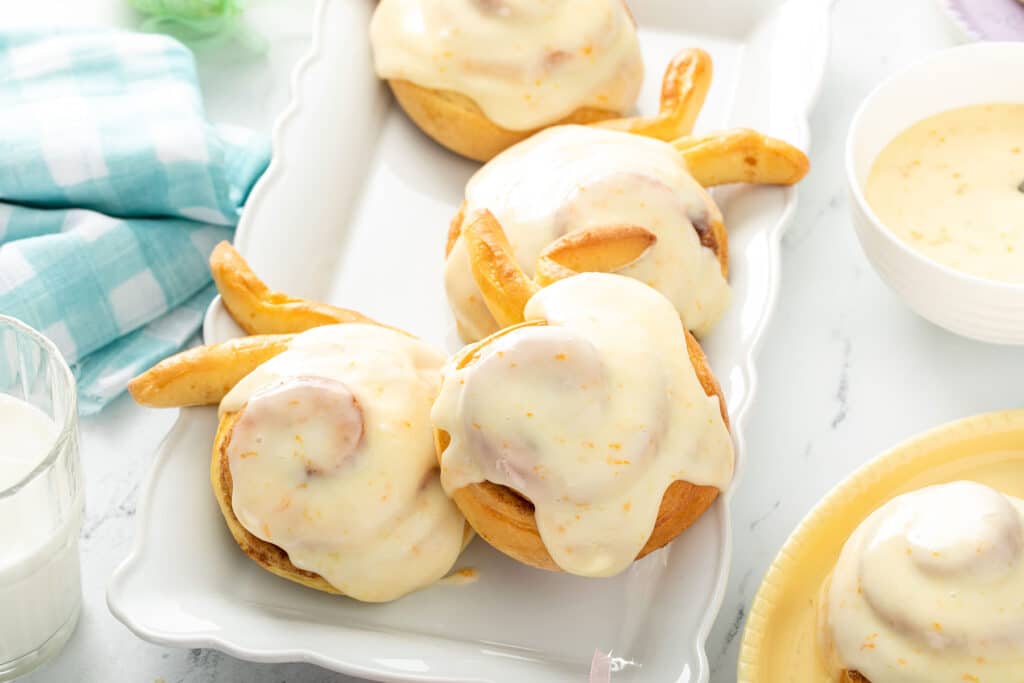 Orange cream cheese glazed cinnamon rolls shaped like Easter bunnies on a white platter