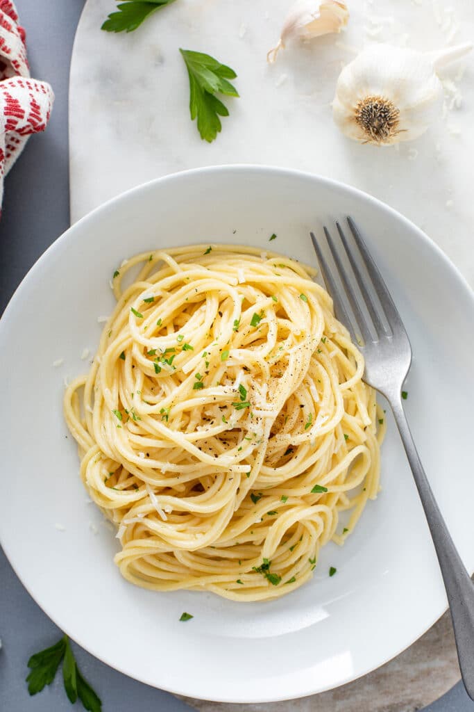 A dinner plate filled with buttered noodles, sprinkled with Parmesan cheese and garnished with chopped parsley.