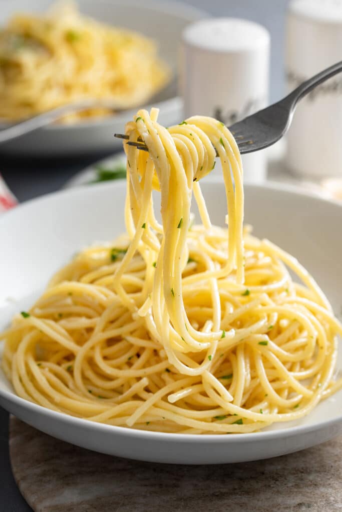 A dinner fork lifting silky buttery noodles from a plate.