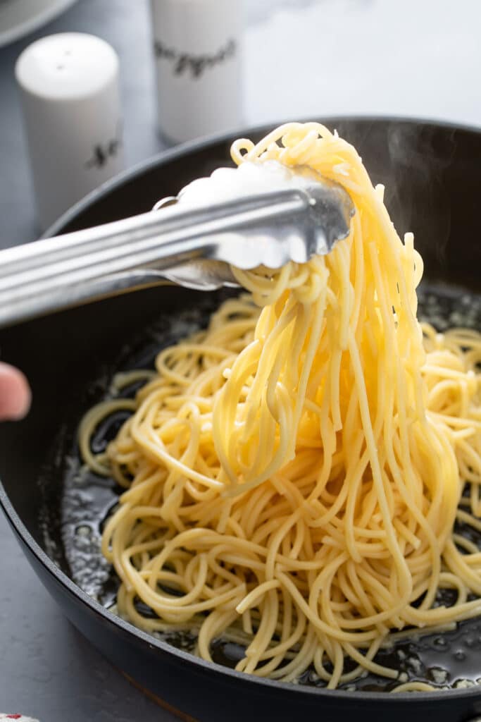 Adding pasta noodles into skillet with garlic butter mixture with tongs 