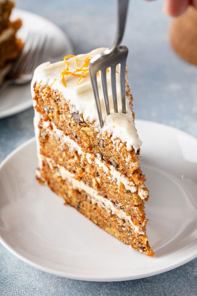 Fork piercing a slice of three-layer carrot cake