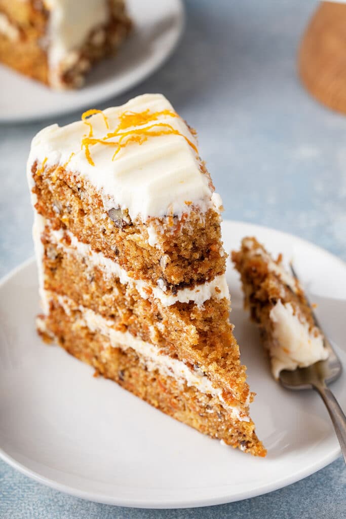 A slice of three-layer homemade carrot cake with orange cream cheese frosting.