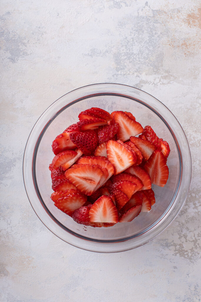 Glass bowl filled with fresh and ripe sliced strawberries.
