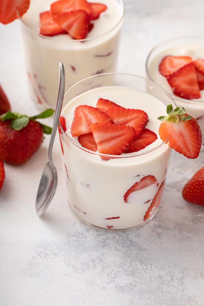 Glass cup filled with a rich creamy sauce and sliced strawberries or fresas con crema dessert.