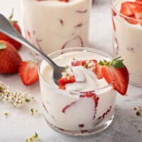 Fresh strawberries sliced and layered with a creamy sauce inside a glass.