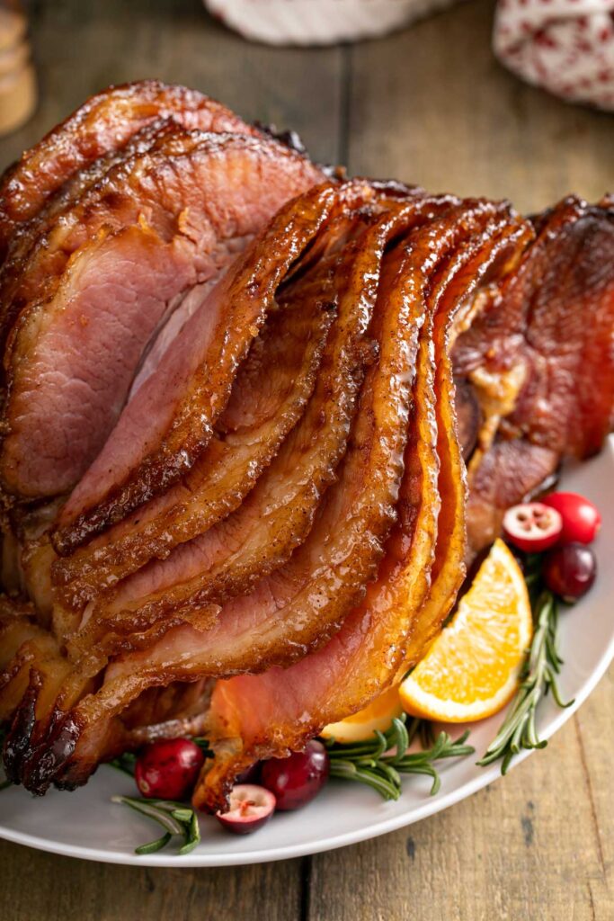 Caramelized slices of a spiral baked ham on a white platter.