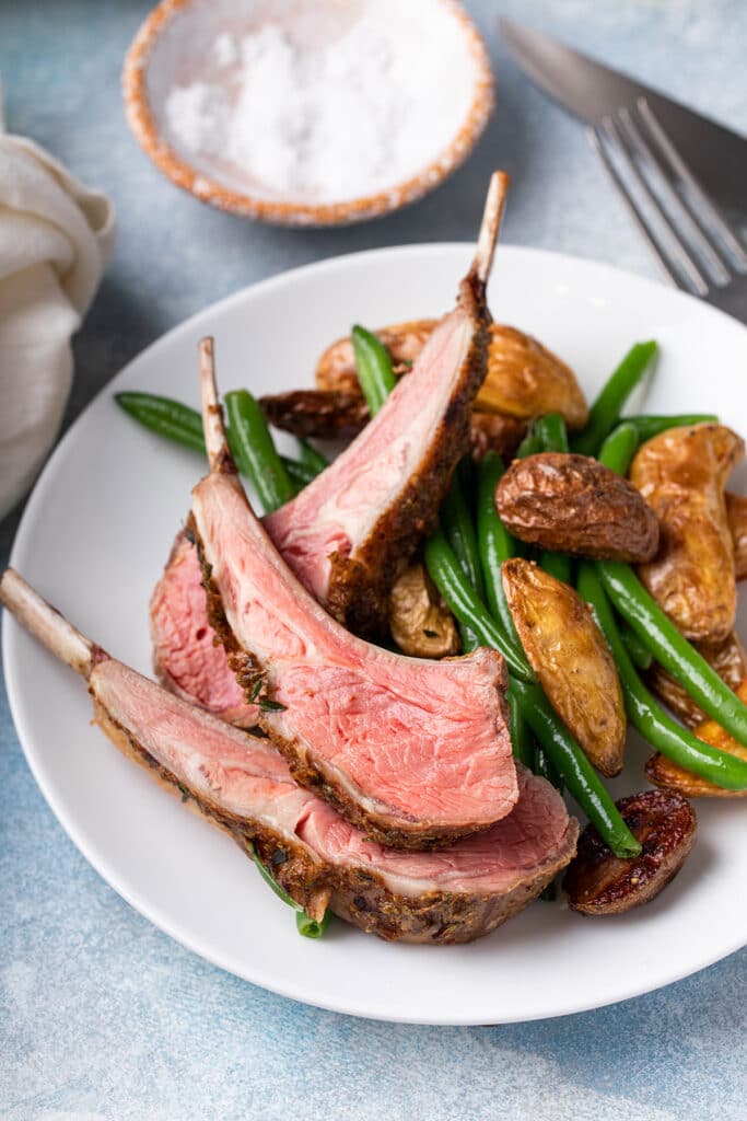 Pink medium-rare lamb ribs from a lamb rack served with roasted potatoes and green beans.