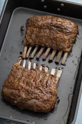 Two cooked racks of lamb coated with an herb and Dijon mustard mixture in a roasting pan.