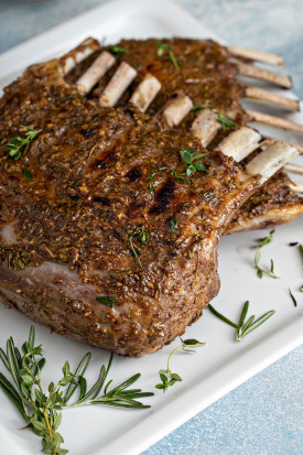 Close view of two golden brown Roasted Lamb Racks on a white plate.