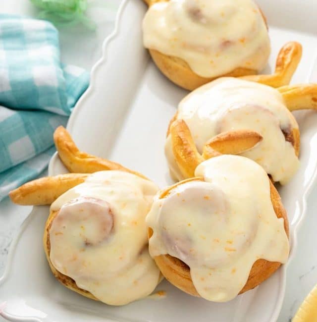 Orange cream cheese glazed cinnamon rolls shaped like Easter bunnies on a white platter