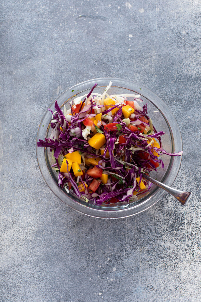 Mango Slaw ingredients mixed in a glass bowl for blackened tacos.