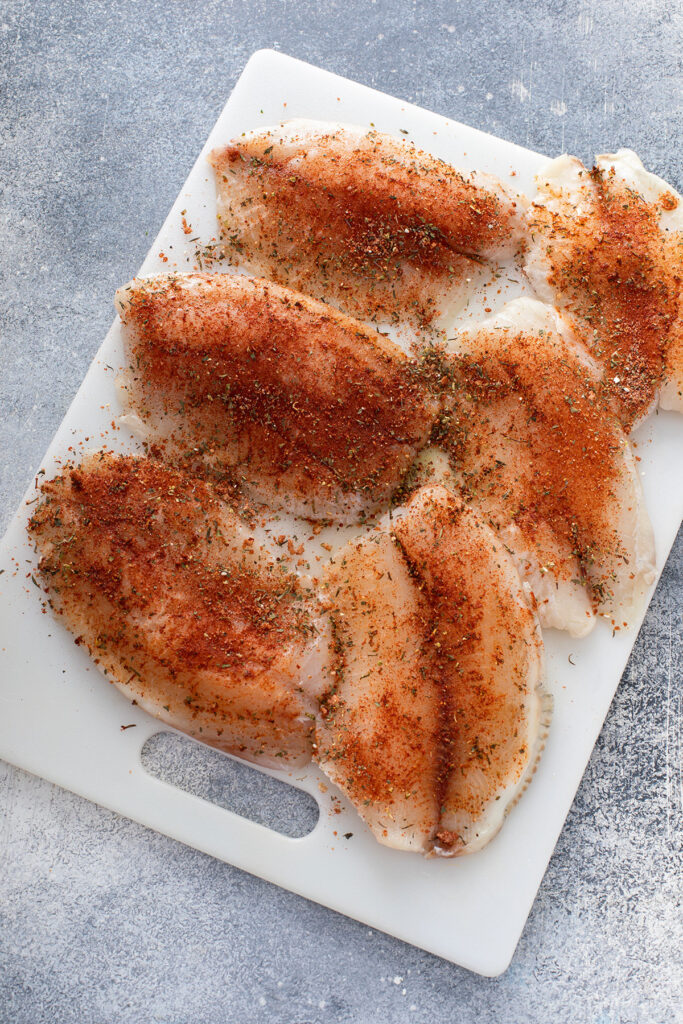 Fish coated in blackened seasoning resting on a cutting board ready to be cooked.