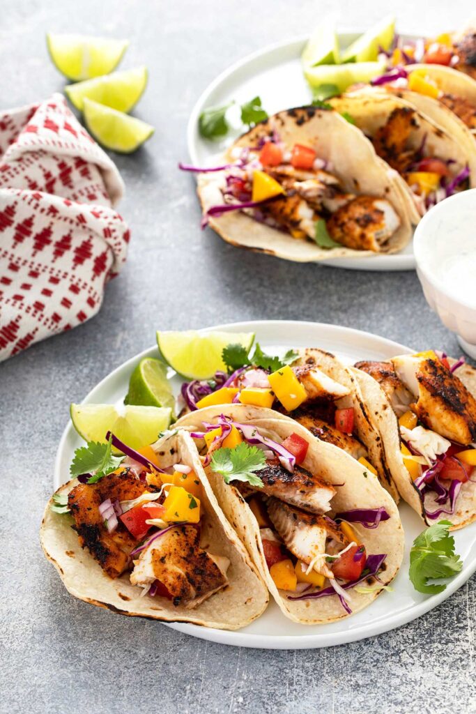 Blackened Fish Tacos with mango slaw, decorated with slices of lime and garnished with cilantro.