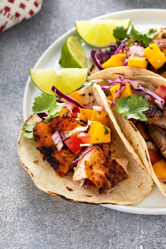Blackened Fish Tacos with mango slaw, decorated with slices of lime and garnished with cilantro.