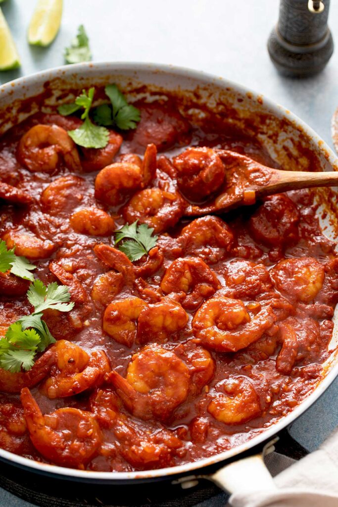 Skillet filled with shrimp tossed in spicy red chile sauce.