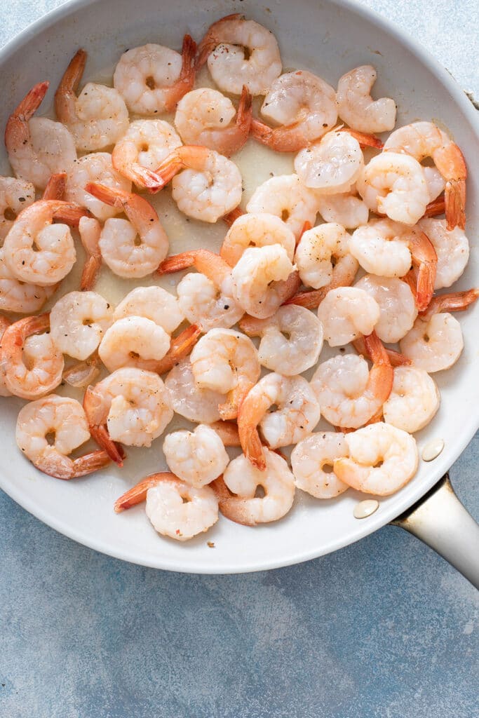 Shrimp in saucepan being cooked and seasoned with lime juice, salt, and pepper. 