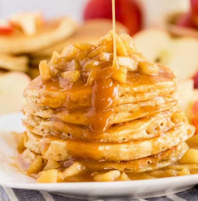 A stack of apple pancakes topped with caramel apples and drizzled with sweet caramel on a white plate