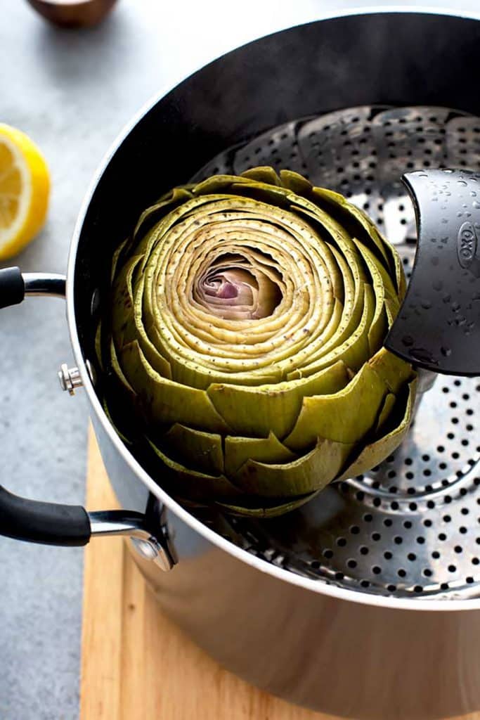 a cooked artichoke in a steaming basket