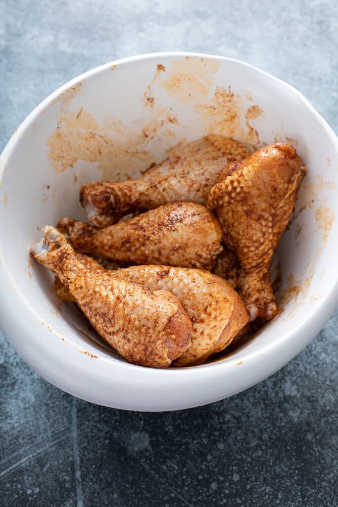 Dry Spiced seasoned raw chicken legs in a white bowl