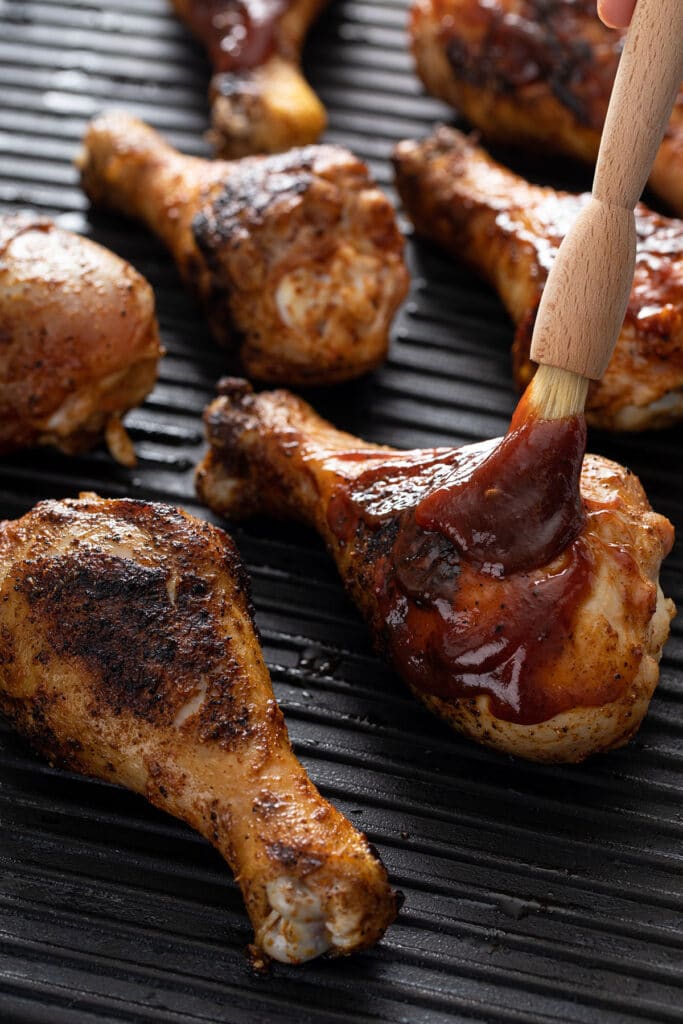 Grilled chicken getting brushed with barbecue sauce,