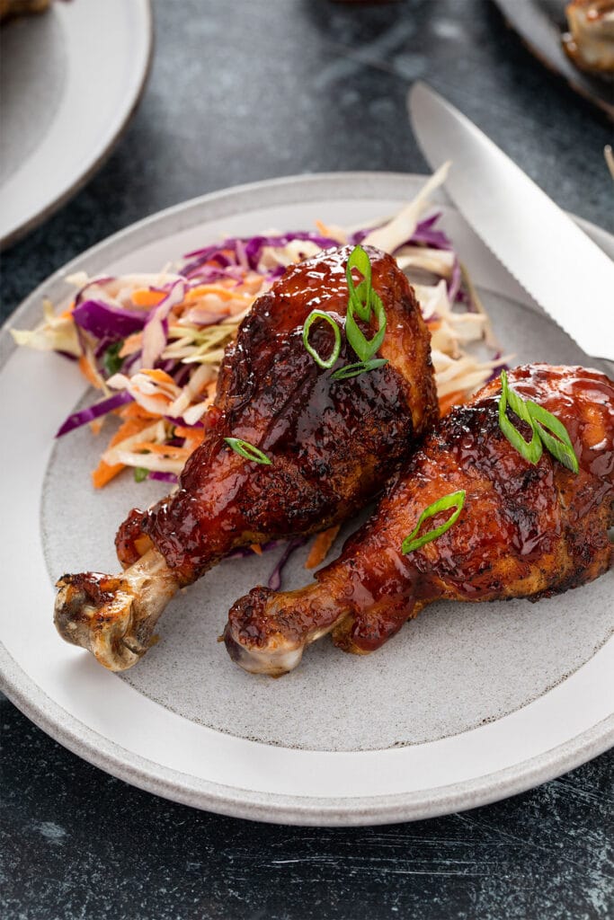 Two grilled chicken drumsticks served with coleslaw on a white plate