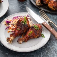 Grilled BBQ chicken legs served with coleslaw on a white plate