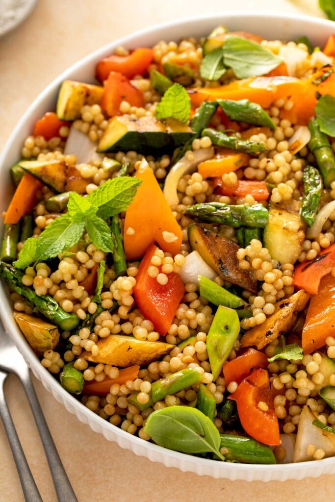 Close up view of a bowl filled with couscous pasta salad with grilled asparagus, bell peppers and summer squash