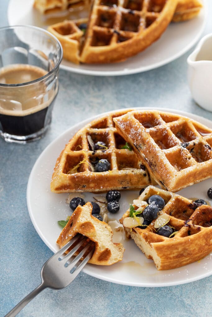 A serving of blueberry and lemon waffles topped with sliced almonds and fresh blueberries