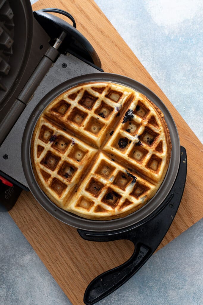 Crispy, golden brown, delicious lemon blueberry waffle ready to be served from waffle iron.  
