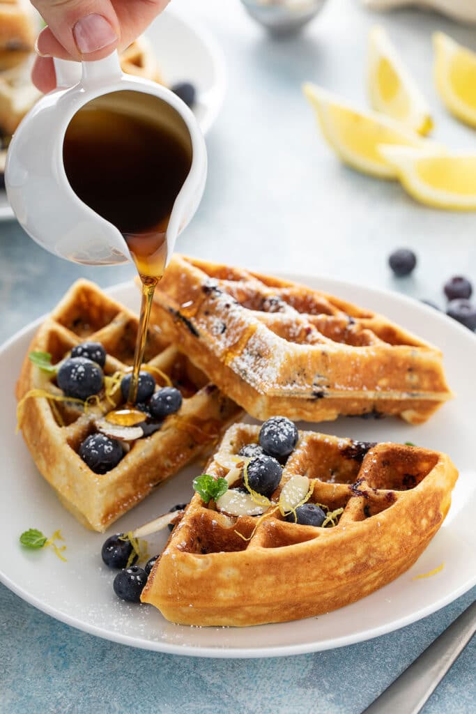 Maple syrup pouring over lemon blueberry waffles.