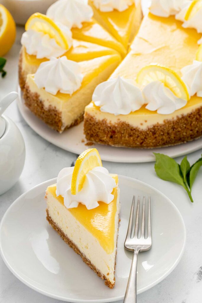 Sliced of cheesecake topped with lemon curd, whipped cream and lemon slices on a white plate.