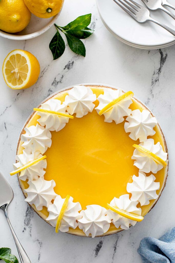 Photo of the top view of a lemon cheesecake decorated with whipped cream and lemon slices.