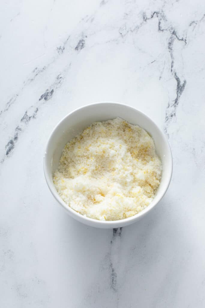 sugar and lemon zest combined in small glass bowl for lemon cheesecake 