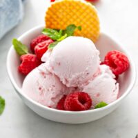 raspberry ice cream scoops in a white bowl garnished with fresh raspberries