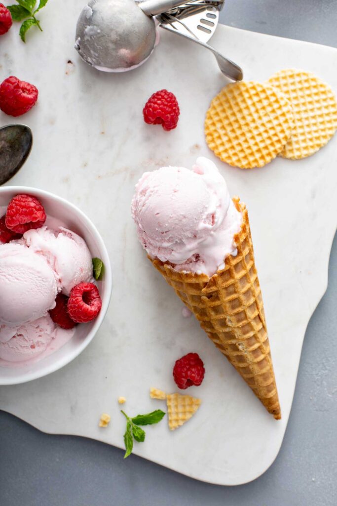 A waffle cone with a scoop of raspberry ice cream.