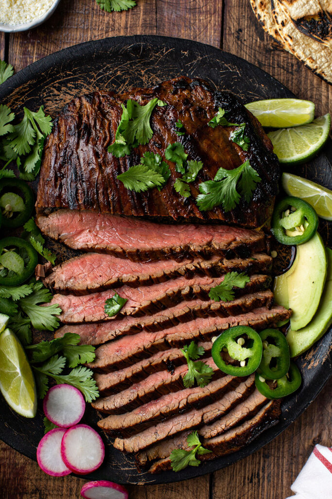 sliced authentic grilled carne asada with cilantro and avocados in a black plate