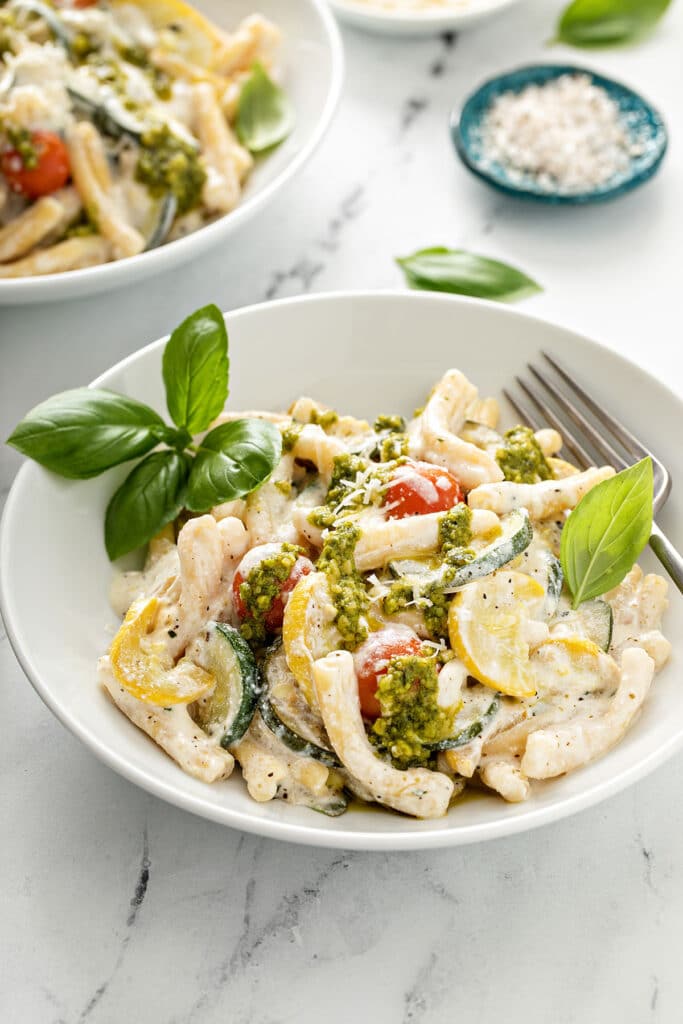 A bowl filled with creamy pasta with summer squash and cherry tomatoes