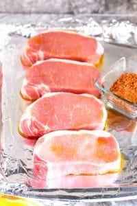 Four pork chops seasoned on a baking sheet covered with aluminum foil