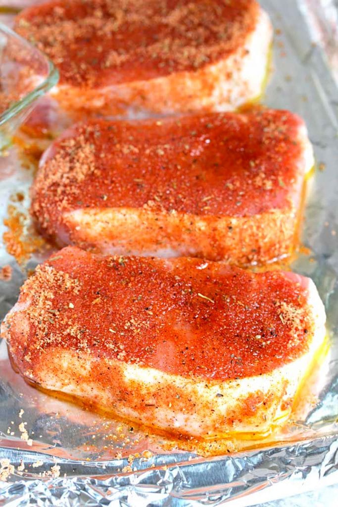 Four seasoned pork chops over a baking tray covered with aluminium foil