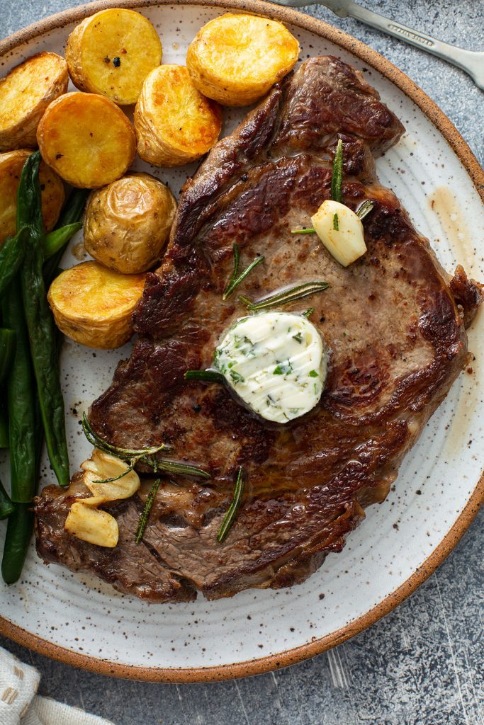 Golden brown seared steak topped with herb butter served with potatoes and green beans.