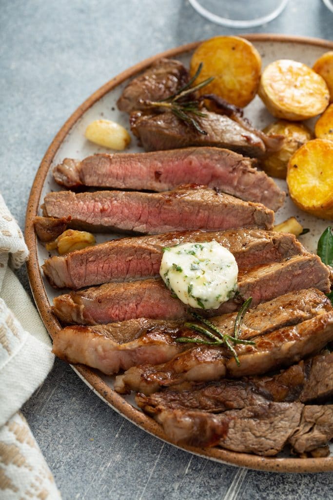 Sliced steak with herb and garlic butter with roasted potatoes on a plate.