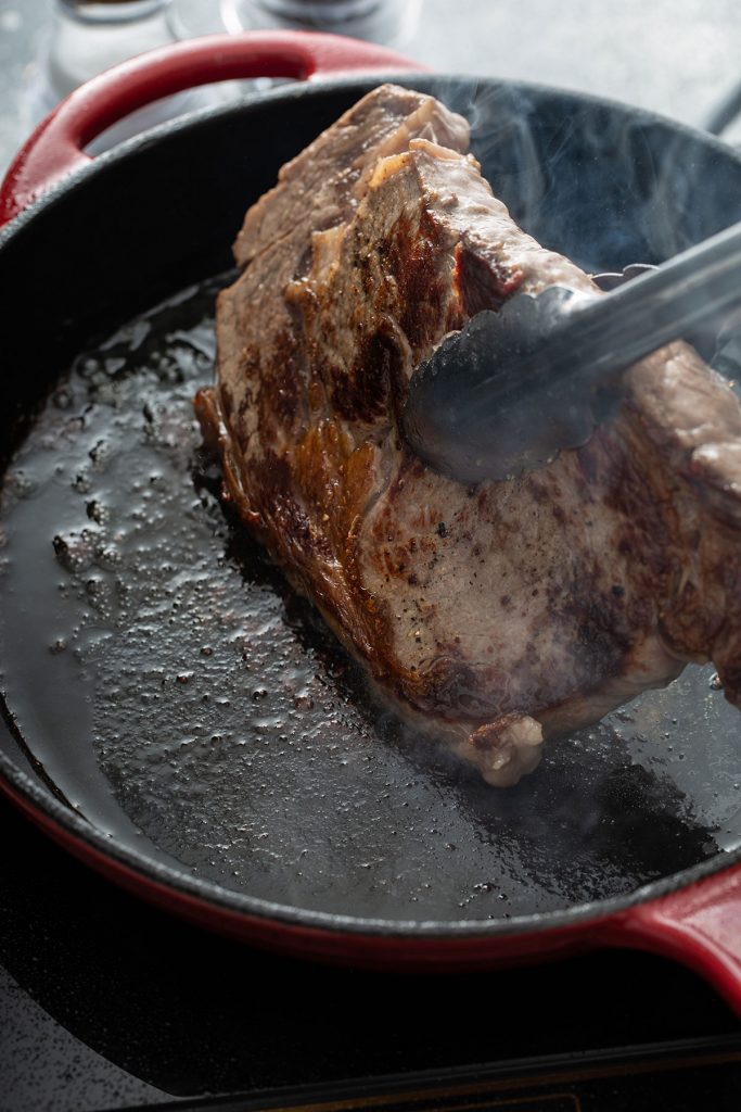 flipping a golden brown steak with tongs