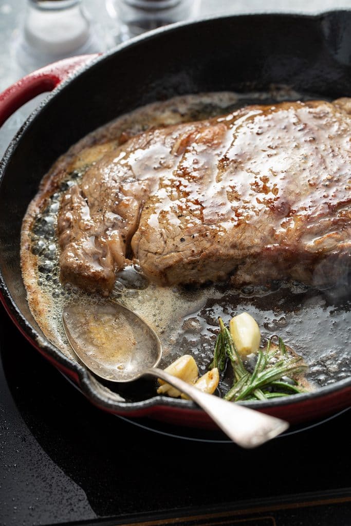 juicy steak cooking with garlic and rosemary on a cast iron skillet
