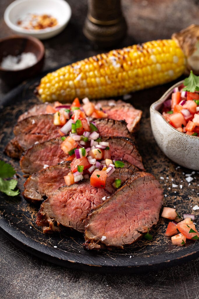 Serving of medim-rare slices of tri tip steak on a plate topped with pico de gallo